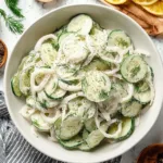 A refreshing creamy cucumber salad in a bowl, garnished with herbs.